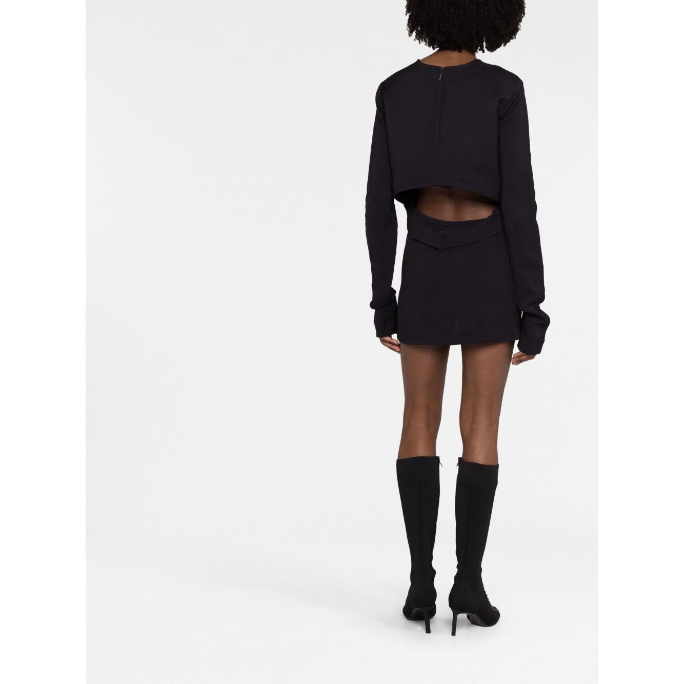 Back view of 032C 'Kicked Back' black short dress with cut-out detail, long sleeves, and straight hem, model wearing knee-high boots.