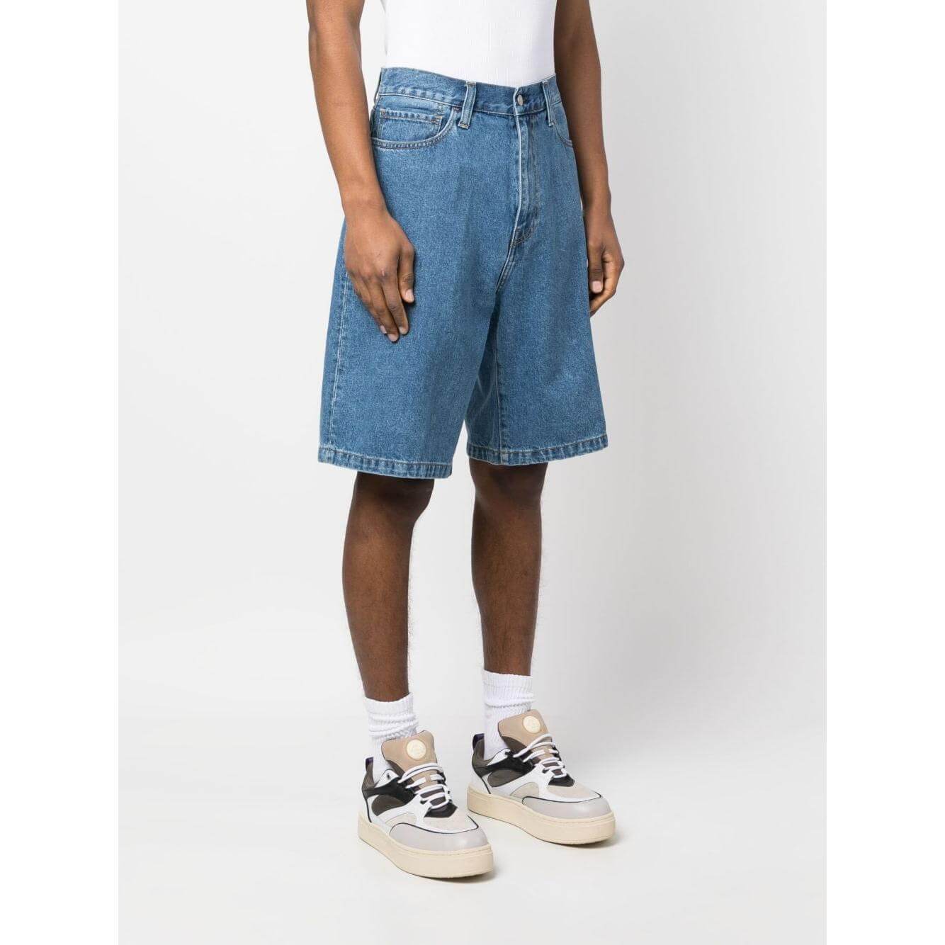 Model wearing Carhartt WIP MAIN blue denim shorts, knee-length, with belt loops and five-pocket design, paired with sneakers.