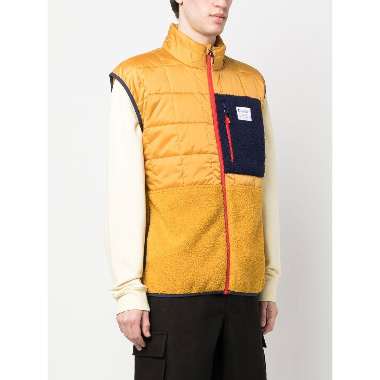 Mustard yellow COTOPAXI padded gilet with chest logo patch, red zip fastening, and sleeveless design worn by a 6ft 1in model in size M.