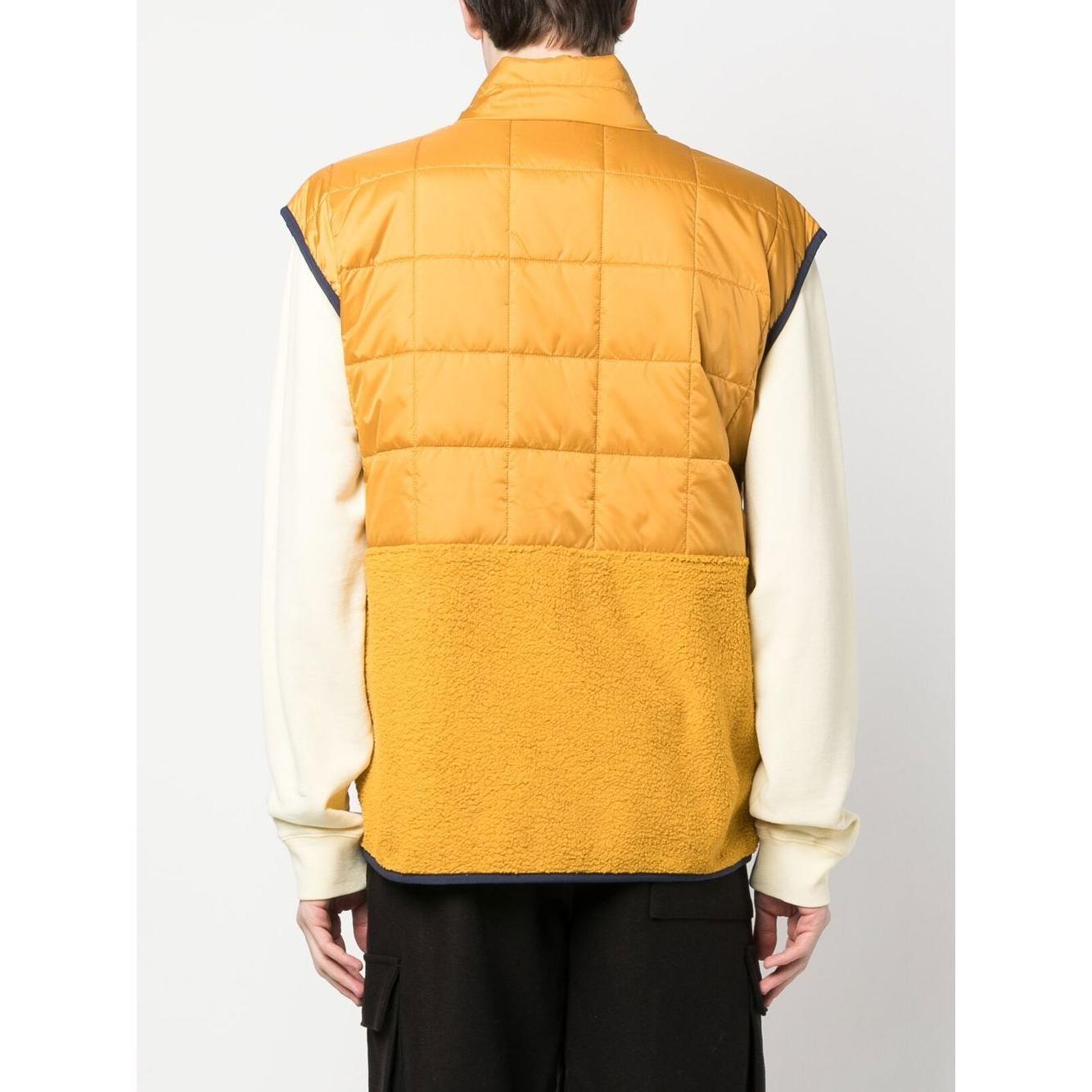 Back view of a mustard yellow COTOPAXI padded gilet with a quilted and fleece hybrid design, sleeveless and worn over a long sleeve shirt.