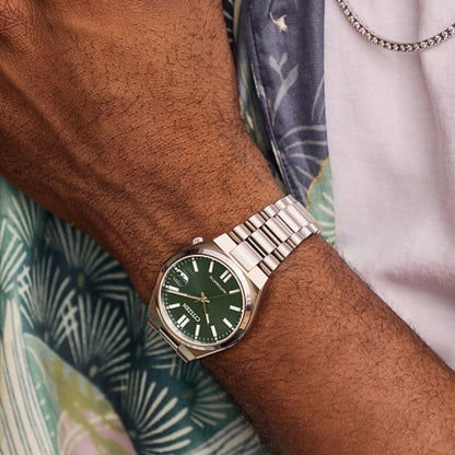 CITIZEN MOD. NJ0200-50X watch with green dial and silver bracelet on wrist against patterned background.