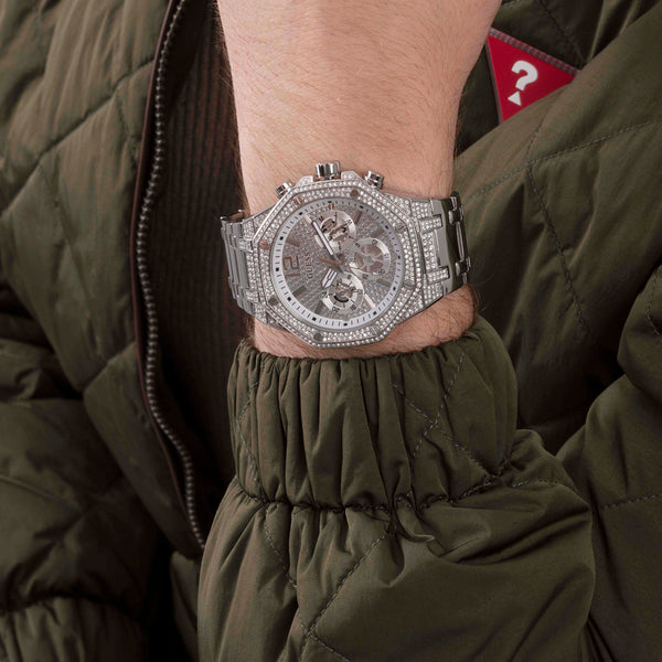 GUESS Mod. MOMENTUM wristwatch with silver strap, worn over a quilted green jacket, showcasing luxurious design and craftsmanship.