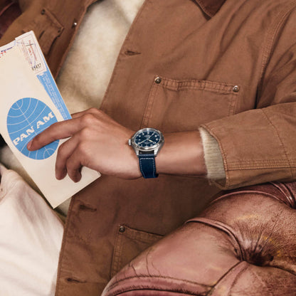 Person wearing TIMEX WATCHES Mod. TW2Y38800, with a vintage airmail envelope, sitting on a leather sofa.